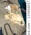 Discarded fishing nets and ropes on dockside with water in background, marine debris visible 135608057