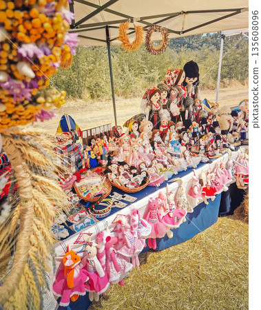 Causeni, Moldova - July 27, 2025: Traditional rustic crafts and rural craftsmanship at an outdoor market. Intricate wheat sheaf arrangements and handmade folk dolls dressed in national costumes 135608096