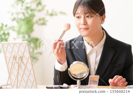 一位身穿職業裝的女大學生正在鏡子前補妝。 135608214