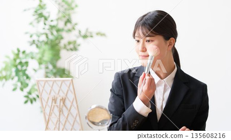 一位身穿職業裝的女大學生正在鏡子前補妝。 135608216