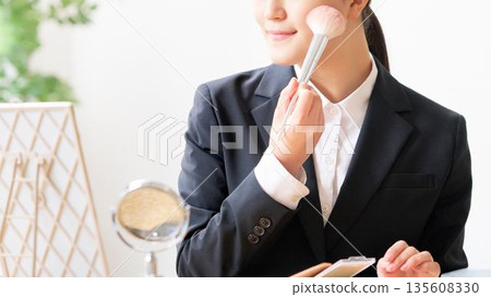一位身穿西裝的女士正用腮紅刷為臉頰增添一抹紅暈。 一位身穿西裝的女士正用腮紅刷為臉頰增添一抹紅暈。 135608330