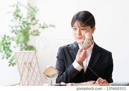 A female university student in a recruitment suit adjusting her makeup in the mirror A female university student in a recruitment suit adjusting her makeup in the mirror 135608331