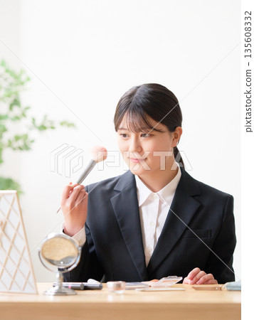 A female university student in a recruitment suit adjusting her makeup in the mirror 135608332