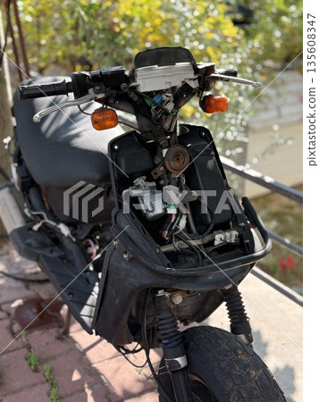 Broken motorcycle with missing front panel and exposed wiring in outdoor urban setting Broken motorcycle with missing front panel and exposed wiring in outdoor urban setting 135608347