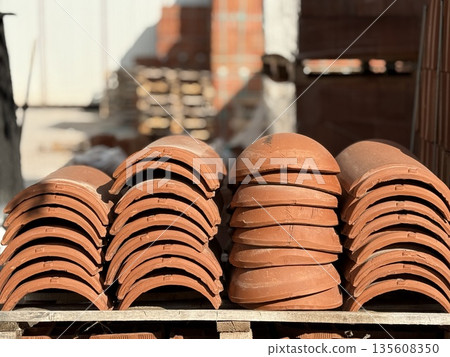 Stacked terracotta roof tiles on pallets in a sunny outdoor construction site Stacked terracotta roof tiles on pallets in a sunny outdoor construction site 135608350