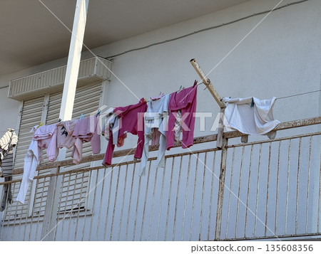 Clothes drying on a balcony rail under sunlight providing a simple urban lifestyle concept Clothes drying on a balcony rail under sunlight providing a simple urban lifestyle concept 135608356