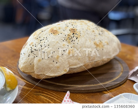 Freshly baked bread loaf with black sesame seeds, placed on wooden board in indoor setting 135608360