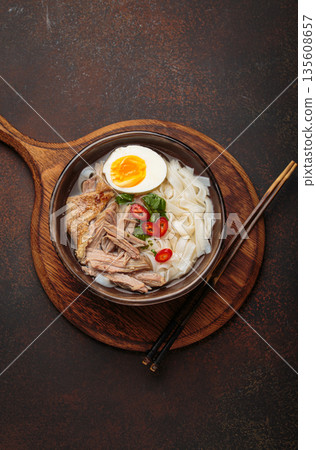 Asian soup rice noodles duck meat egg chopsticks ramen bowl dark rustic background 135608657