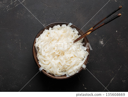 Rice cooked plain noodles with chopsticks dark bowl top view black rustic background 135608669