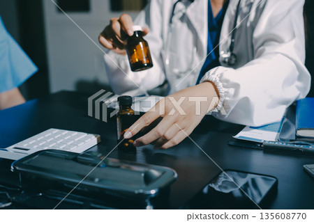 Female doctor holding a medicine bottle is checking the quality of medicine for any side effects the patient or not and recording patient information at the hospital. medical and health care concept Female doctor holding a medicine bottle is checking the quality of medicine for any side effects the patient or not and recording patient information at the hospital. medical and health care concept 135608770