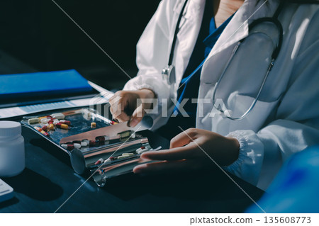 Female doctor holding a medicine bottle is checking the quality of medicine for any side effects the patient or not and recording patient information at the hospital. medical and health care concept Female doctor holding a medicine bottle is checking the quality of medicine for any side effects the patient or not and recording patient information at the hospital. medical and health care concept 135608773
