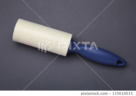 Cloth fabrics cleaner lint roller brush with paper roll on blue background. Sticky roller, pet cat dog fur dust hair remover Cloth fabrics cleaner lint roller brush with paper roll on blue background. Sticky roller, pet cat dog fur dust hair remover 135610015