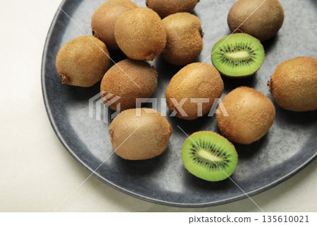 Green kiwi on plate on light background. Tropical fruit. 135610021