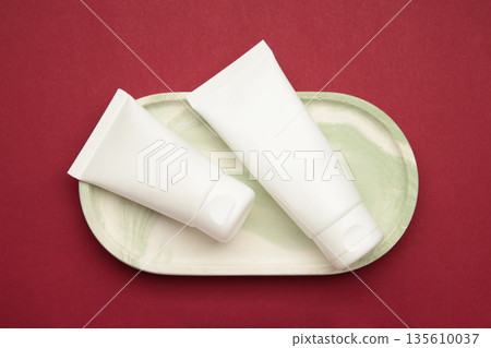 White plastic cosmetic tubes on plate on red background. Space for text White plastic cosmetic tubes on plate on red background. Space for text 135610037