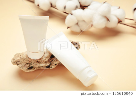 White cream tube on stone with cotton flower on beige background. Skincare handmade beauty product. White cream tube on stone with cotton flower on beige background. Skincare handmade beauty product. 135610040