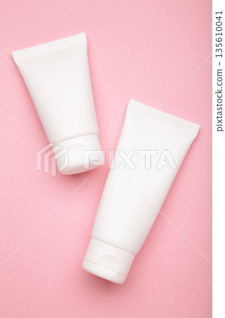 White plastic cosmetic tubes on pink background. Vertical photo 135610041