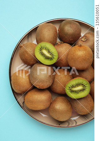 Green kiwi on plate on blue background. Tropical fruit. Vertical photo Green kiwi on plate on blue background. Tropical fruit. Vertical photo 135610051