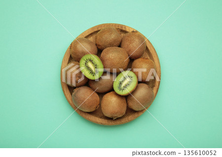 Green kiwi on wooden plate on mint background. Tropical fruit. Green kiwi on wooden plate on mint background. Tropical fruit. 135610052