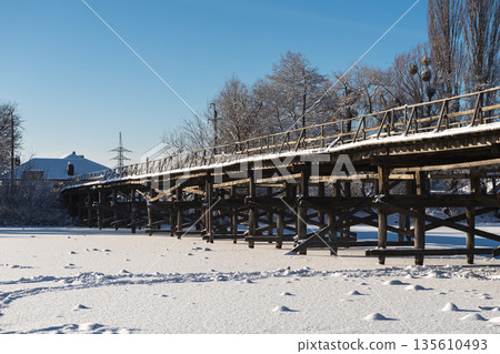 Beautiful winter landscape with a frozen pond and snow-covered wooden bridge on a clear sunny day 135610493