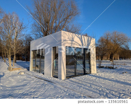 A small glass and concrete building, a kiosk or pavilion in the middle of a winter park A small glass and concrete building, a kiosk or pavilion in the middle of a winter park 135610561
