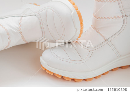 Pair of stylish white winter boots with orange soles placed on white background, showing stitched contours. Concept of modern symmetry, Cloud Dancer trend and sleek urban fashion Pair of stylish white winter boots with orange soles placed on white background, showing stitched contours. Concept of modern symmetry, Cloud Dancer trend and sleek urban fashion 135610898