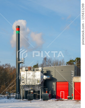 Modern wood chip boiler house with biomass heating system and chimney in winter landscape Modern wood chip boiler house with biomass heating system and chimney in winter landscape 135611299