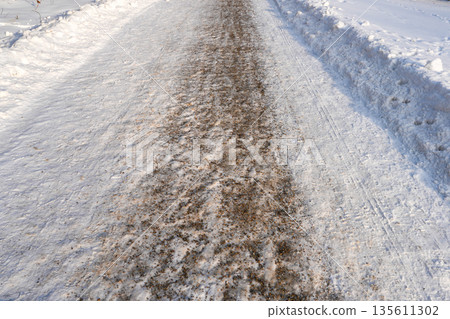 Snowy winter walkway covered with anti-slip gravel for pedestrian safety in icy conditions Snowy winter walkway covered with anti-slip gravel for pedestrian safety in icy conditions 135611302