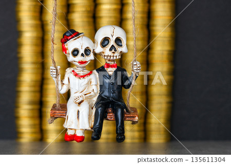 Skeleton couple figurine on swing with stacked gold coins background symbolizing love and wealth 135611304