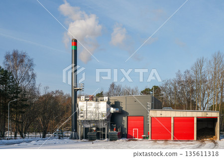 Modern biomass boiler house with wood chip heating plant and smokestack in winter Modern biomass boiler house with wood chip heating plant and smokestack in winter 135611318