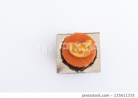 Orange colored pastry with smooth glaze and a fresh orange slice on top, citrus dessert concept Orange colored pastry with smooth glaze and a fresh orange slice on top, citrus dessert concept 135611335