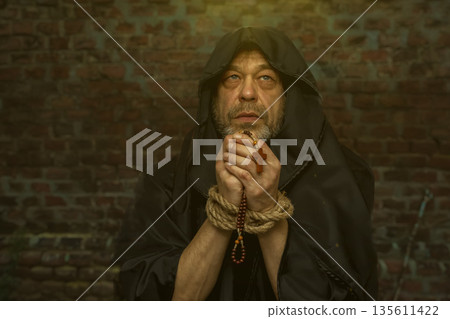 Monk holds rosary with bound hands and raises gaze during prayer. 135611422