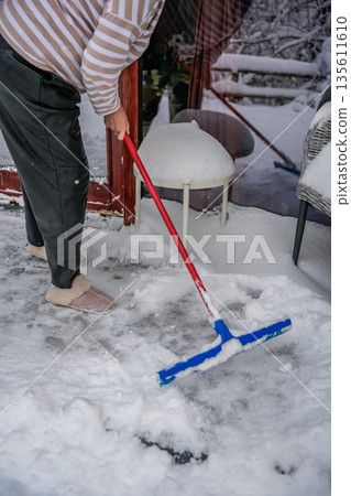 Woman Sweeping Snow on Wooden Cabin Porch 135611610