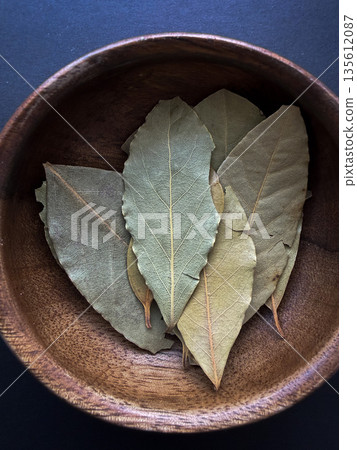 Dried Bay Leaves in Rustic Wooden Bowl on Dark Background 135612087