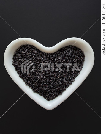 Black Poppy Seeds in Heart-Shaped Bowl on Dark Background Black Poppy Seeds in Heart-Shaped Bowl on Dark Background 135612186
