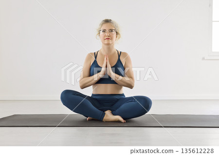 Serene woman practicing yoga meditation in lotus pose with prayer hands indoors Serene woman practicing yoga meditation in lotus pose with prayer hands indoors 135612228
