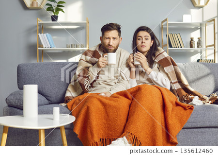 Man and woman are at home in living room, wrapped in warm blanket and feeling flu symptoms. 135612460