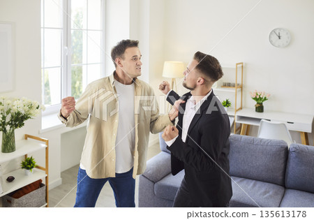 Two men facing off in tense argument with raised fists, threatening physical fight 135613178