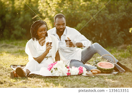 Carefree, relaxed couple enjoying the picnic together. Man and woman tasting red wine from glasses. Carefree, relaxed couple enjoying the picnic together. Man and woman tasting red wine from glasses. 135613351