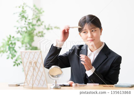 A woman in a recruitment suit checking her appearance by adjusting her bangs with a comb while looking in the mirror A woman in a recruitment suit checking her appearance by adjusting her bangs with a comb while looking in the mirror 135613868