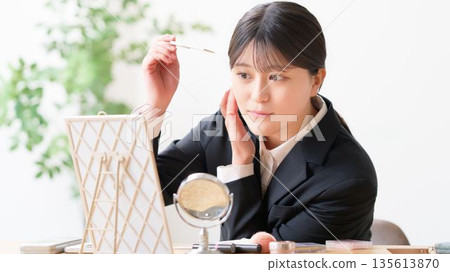 一位穿著招募套裝的女士正在照鏡子，用梳子整理瀏海，檢查自己的儀容。 135613870
