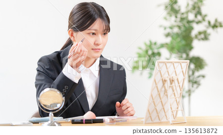 一位身穿西裝的年輕女子正在對著鏡子化妝。 135613872