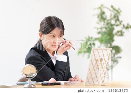 A woman in a suit looking in the mirror and applying eyeliner to enhance the look of her eyes A woman in a suit looking in the mirror and applying eyeliner to enhance the look of her eyes 135613873