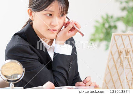 A woman in a suit looking in the mirror and applying eyeliner to enhance the look of her eyes A woman in a suit looking in the mirror and applying eyeliner to enhance the look of her eyes 135613874