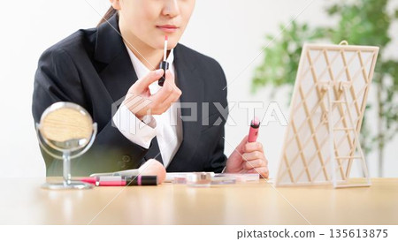 一位穿著西裝的女士正在對著鏡子塗口紅、整理儀容。 135613875