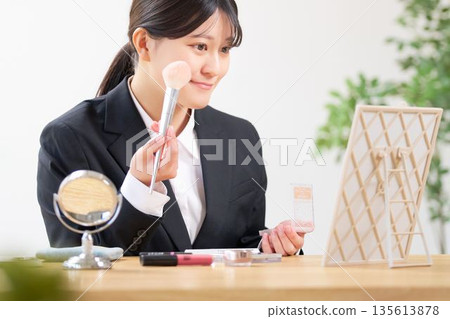 A female university student in a recruitment suit adjusting her makeup in the mirror 135613878