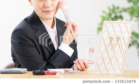 一位身穿西裝的女士正用腮紅刷為臉頰增添一抹紅暈。 135613879