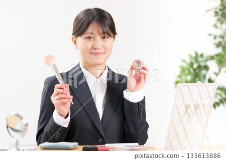 A female university student in a recruitment suit holding makeup tools and introducing them with a smile 135613886