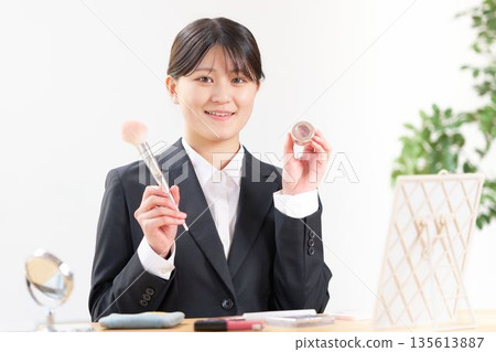 A female university student in a recruitment suit holding makeup tools and introducing them with a smile 135613887