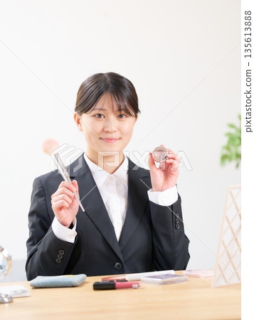 A female university student in a recruitment suit holding makeup tools and introducing them with a smile 135613888
