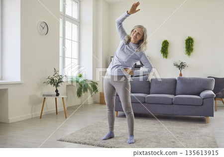Happy senior woman doing physical exercise, side bends and stretching workout Happy senior woman doing physical exercise, side bends and stretching workout 135613915